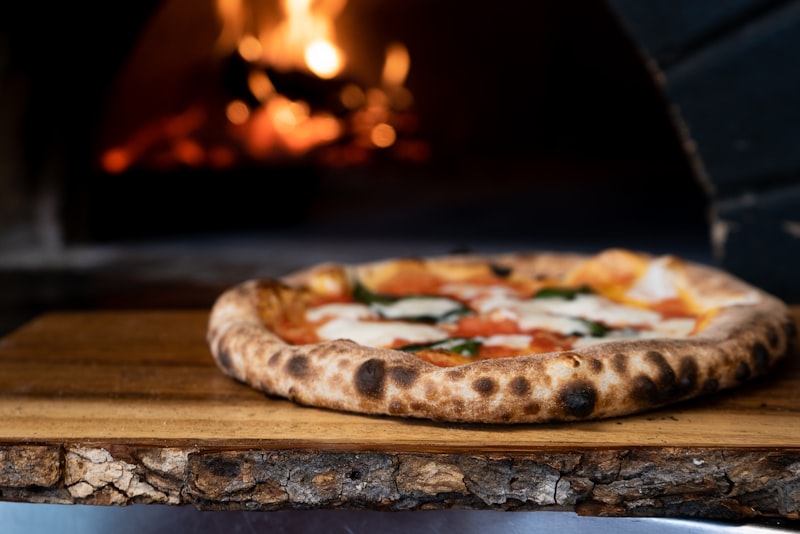 Chefs hand placing wood into stone oven with glowing hot coals